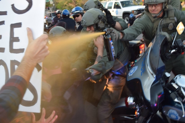 Eager cop sprays protesters from behind motorcycles