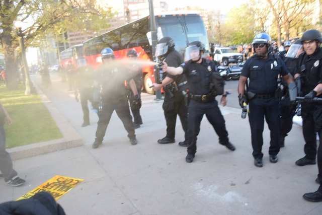 Police spraying a small group of people on the sidewalk.